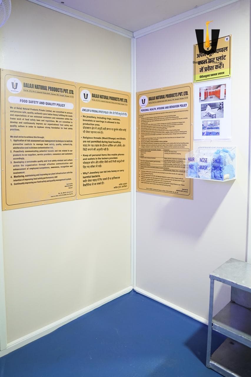 Food safety, jewellery, and hygiene policy boards with a PPE dispenser at plant entry