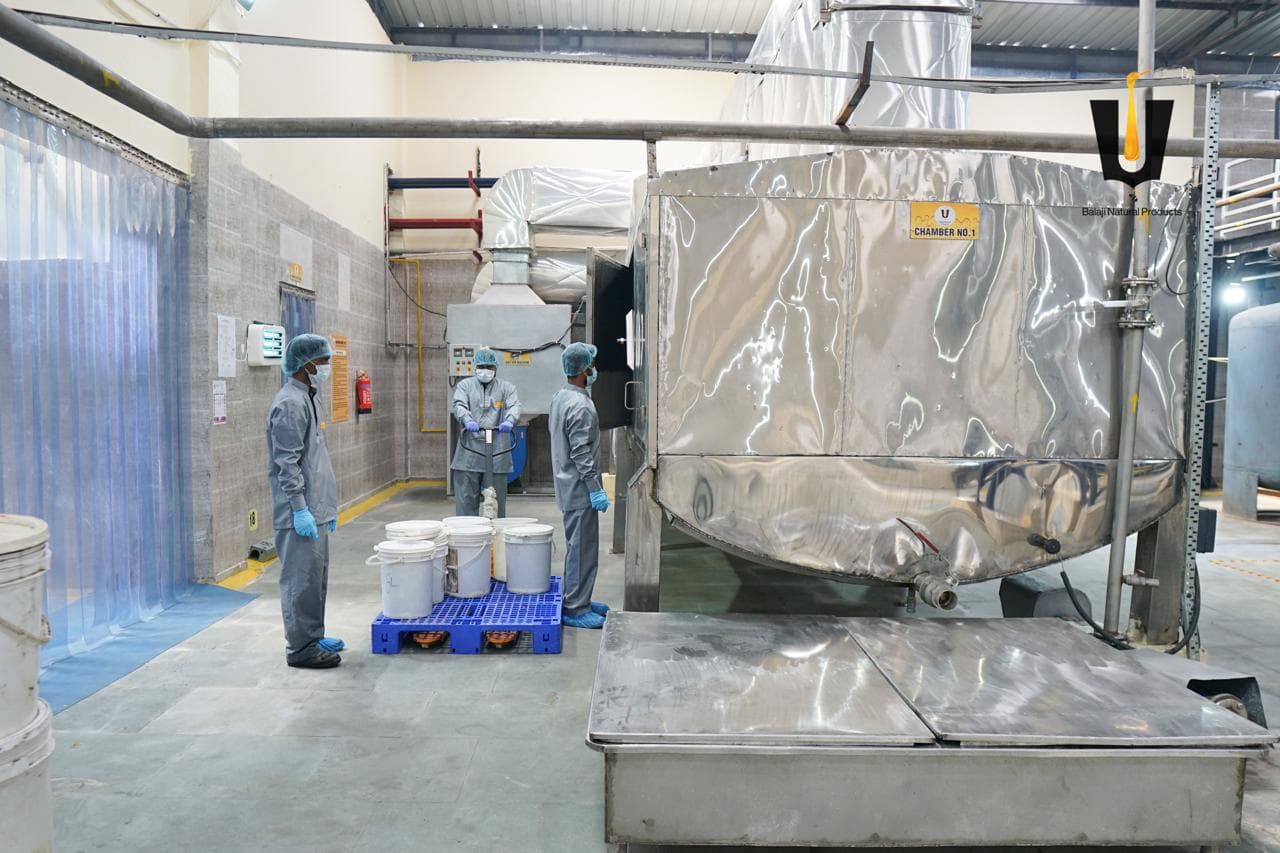 Three workers in PPE with a pallet of honey buckets beside stainless Chamber No. 1
